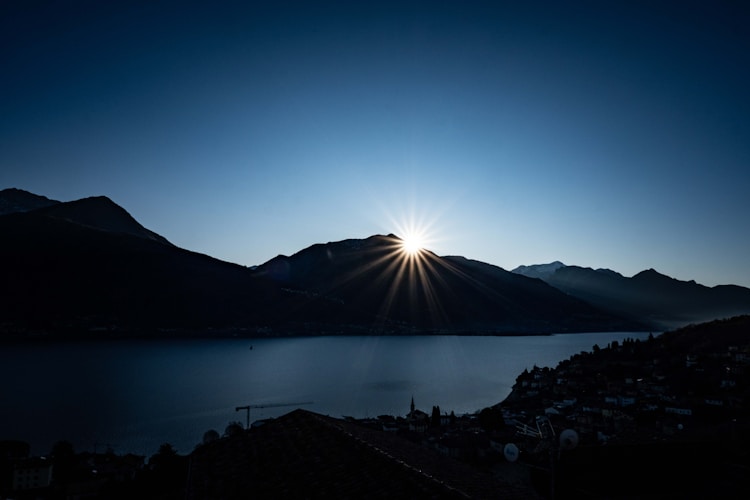 The sun is setting over a lake with mountains in the background