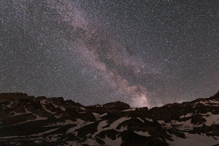 The night sky is filled with stars above a mountain range