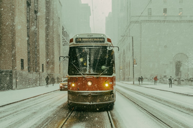 A train traveling down a snowy street next to tall buildings