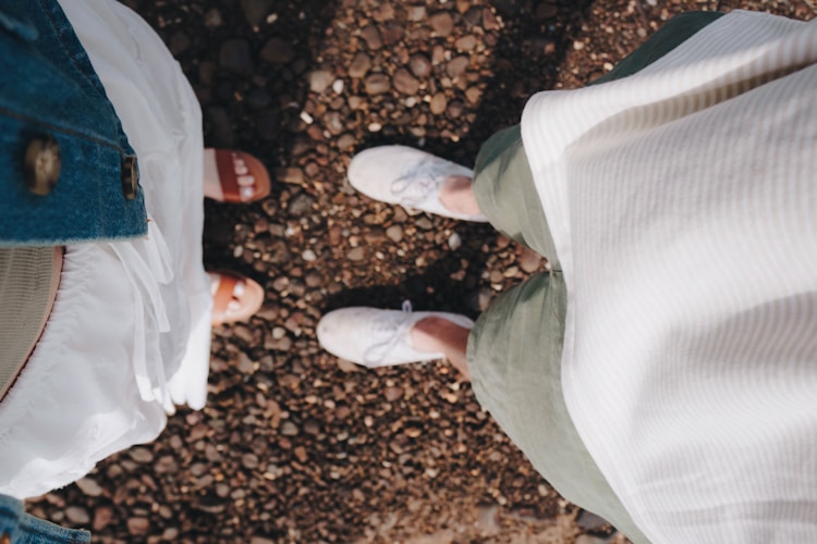 Two people's feet stand on a gravel surface.