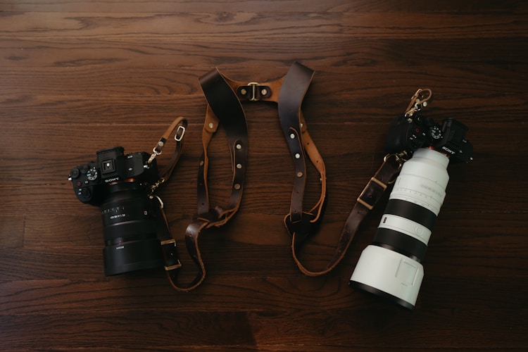 Cameras and a leather camera strap on wood.