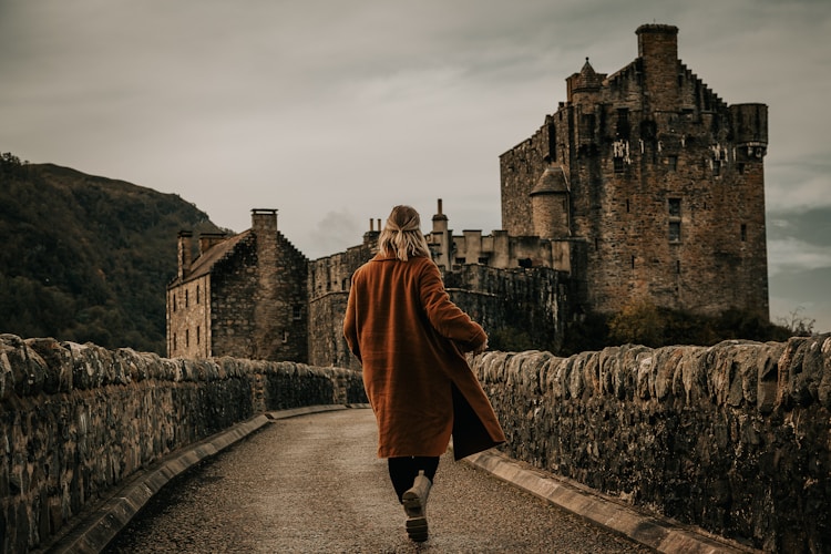 Woman walks toward castle over a stone bridge.