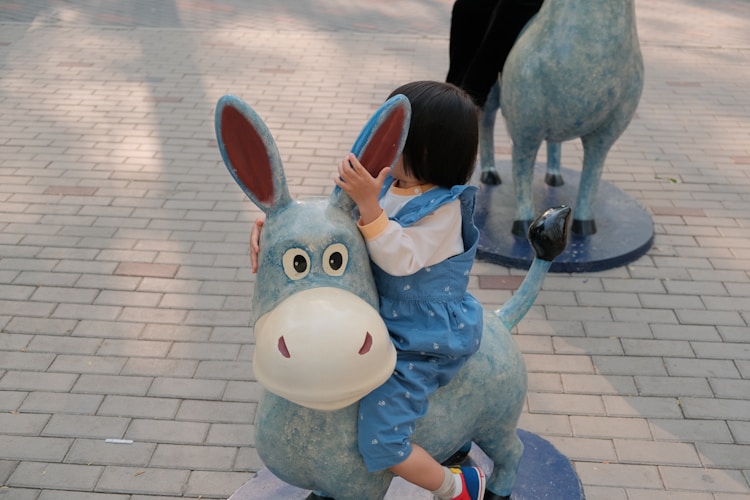 A little girl rides a donkey statue.