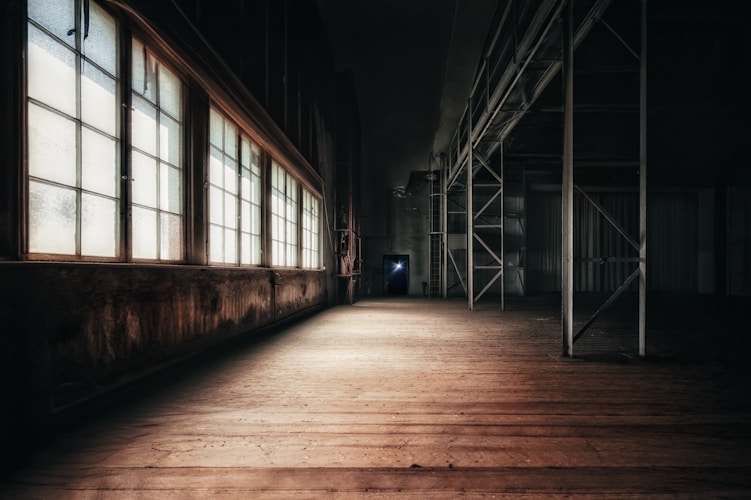 A dark, abandoned warehouse with bright windows.