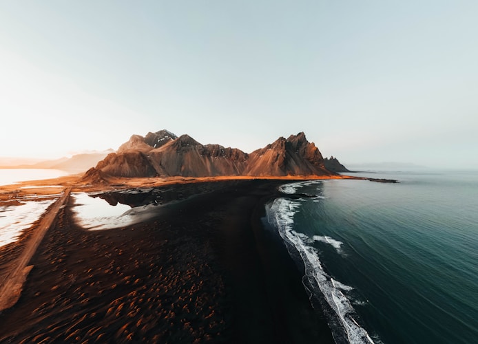 A black sand beach meets the ocean and mountains.