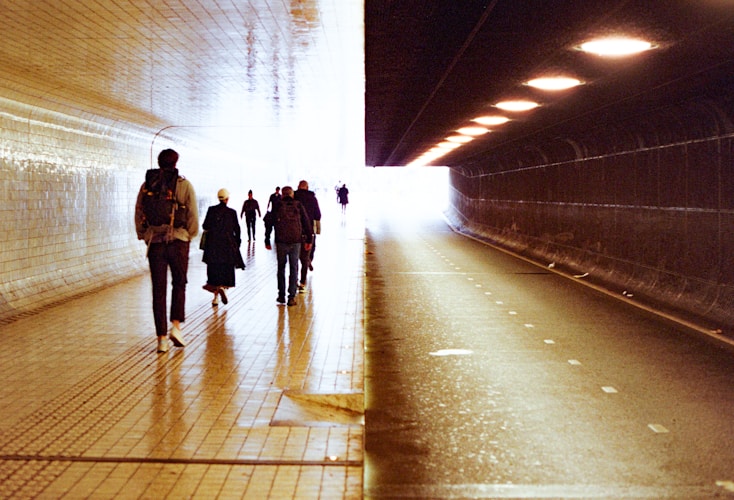 People walk through a tunnel towards bright light.