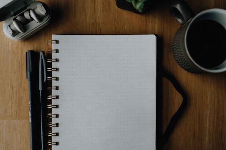 Notebook, pen, headphones, and coffee on a wooden desk.
