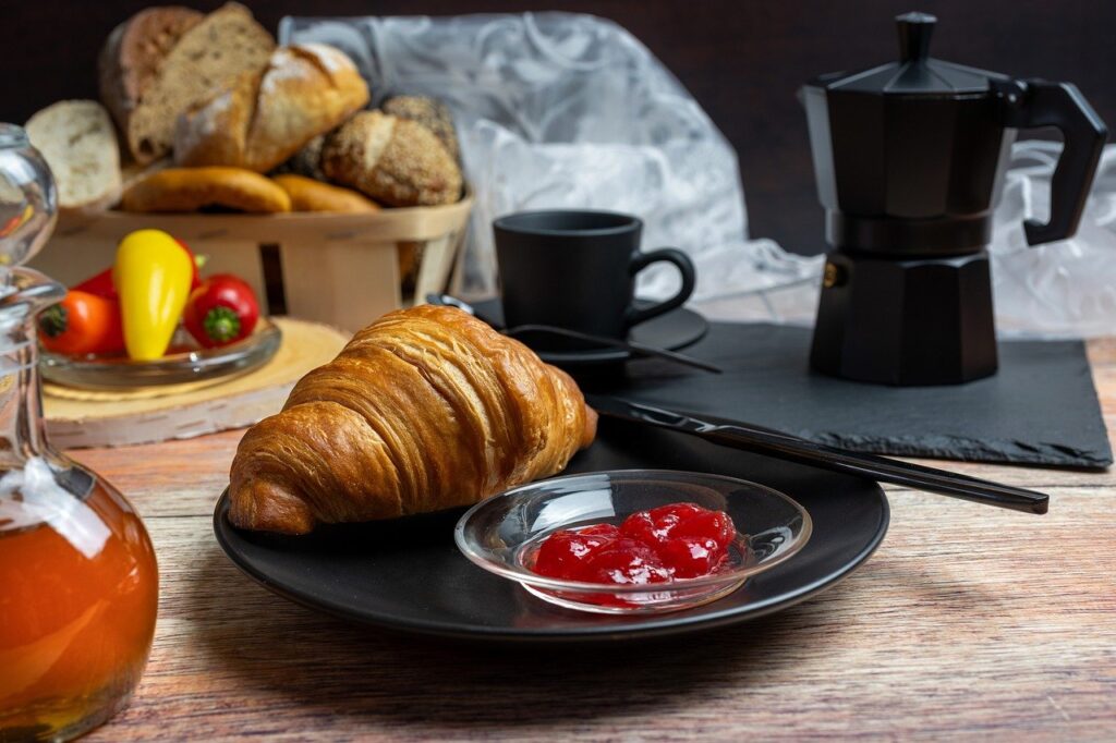 breakfast, croissant, jam, honey, coffee machine, coffee pot, black dishes, bread basket, bun, paprika, tomatoes, rustic table, baked goods, morning meal, mediterranean, comfortable, food scene, enjoyment, café atmosphere